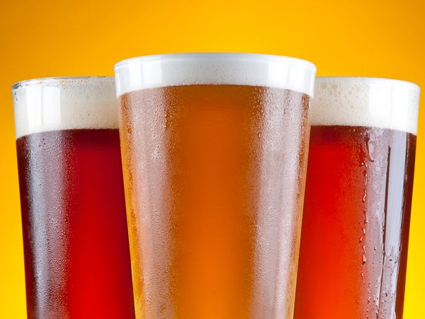 Three glasses of beer with foam on top.