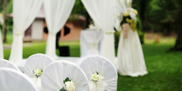 Outdoor wedding setup with white chairs and floral decorations.