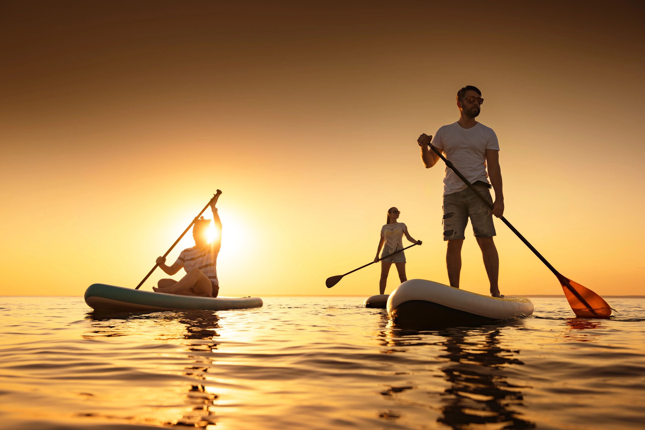 Three people paddleboarding on calm water during a golden sunset.