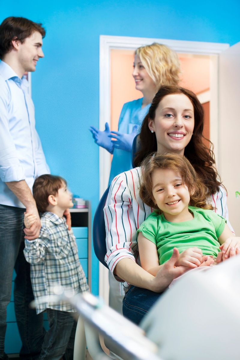 Portrait of an family with two children with their family dentist in the dentist's office. Father and his son talking to female dentist, mother and daughter sitting at dentist's chair and looking at camera and smiling.