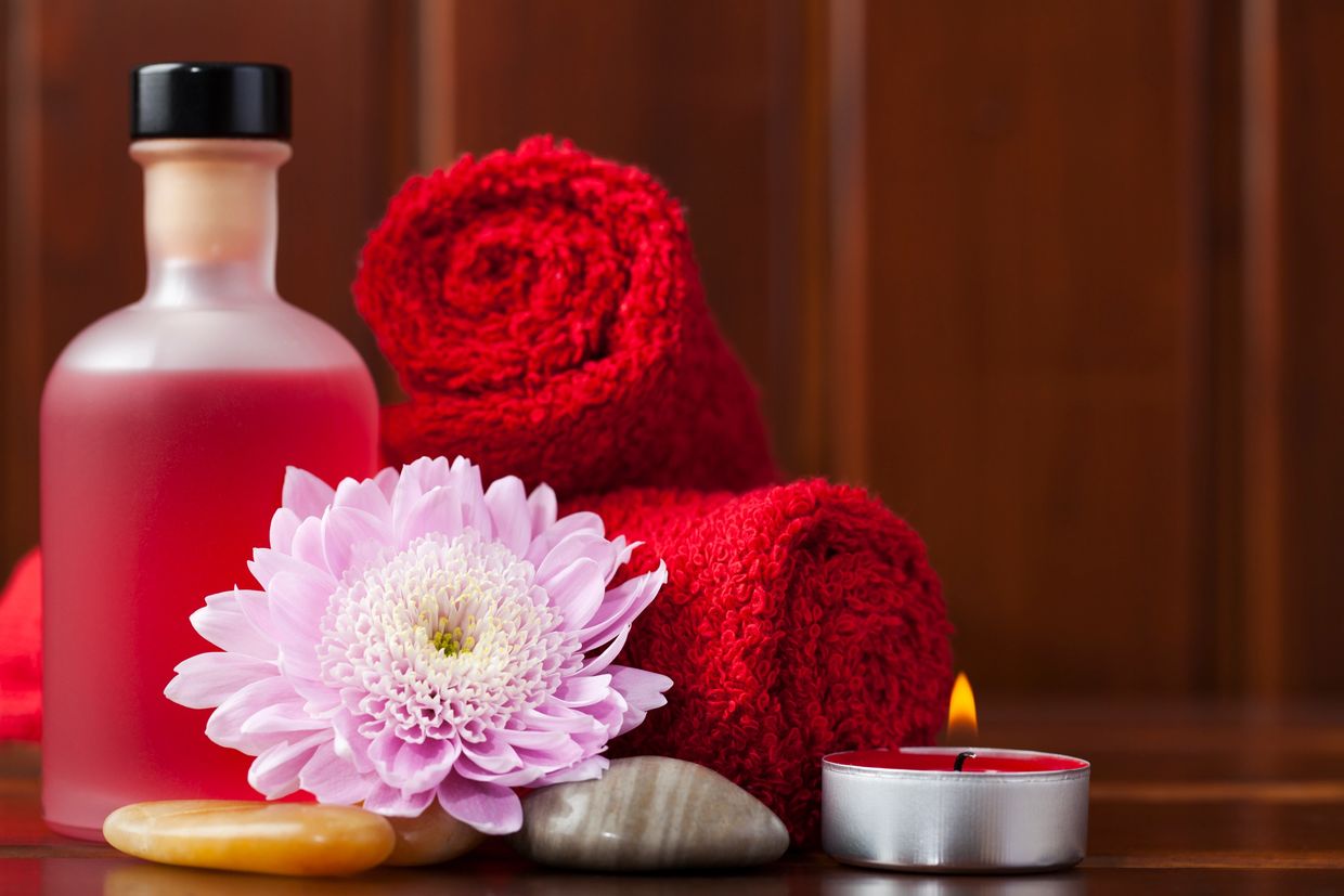 Spa essentials with red towels, pink flower, and candle.