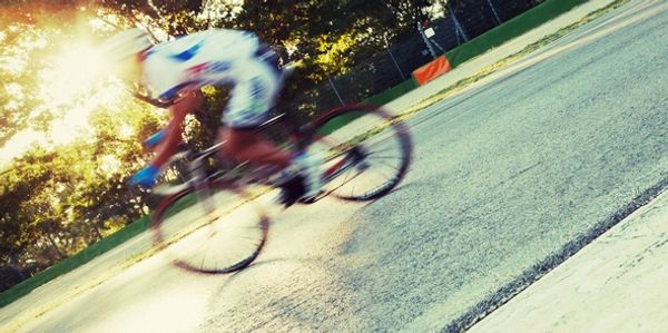 Blurred cyclist speeding on a sunlit road with trees in the background.