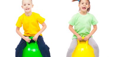 Two children bouncing on colorful space hoppers with joy.