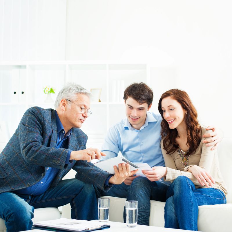 Young Couple Meeting With Senior Financial Advisor presenting new bank offers and investments on digital tablet PC. Senior Financial Advisor pointing with hand to some new offers.