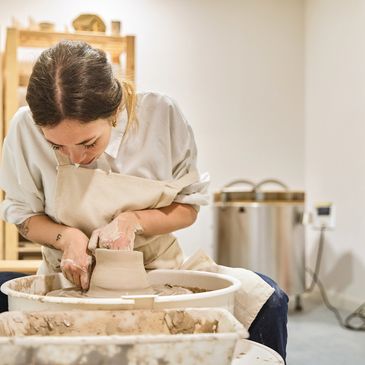 Woman focused on shaping clay on a pottery wheel.