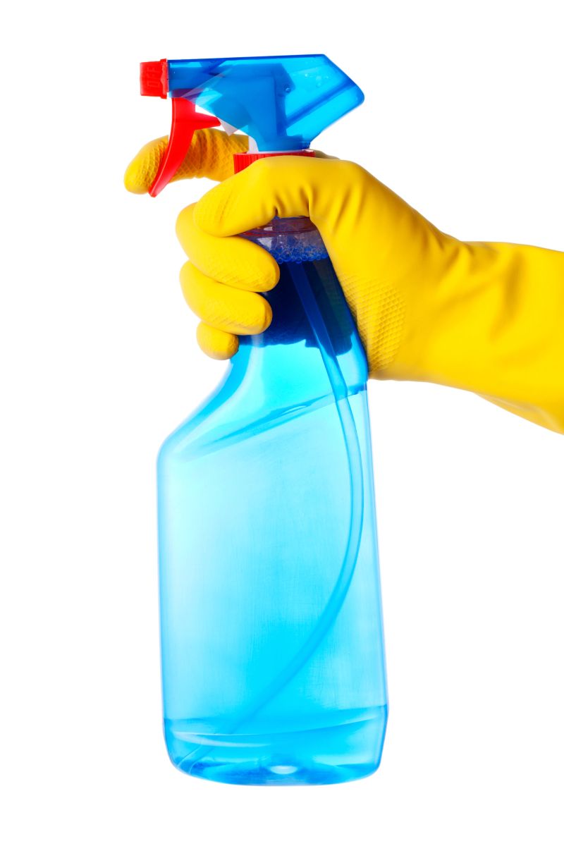 Hand in protective glove holding cleaning spray bottle. Isolated on white.