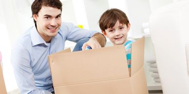 A man and a boy happily unpacking a cardboard box together.