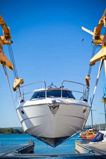 A white yacht being lifted by yellow cranes at a marina.