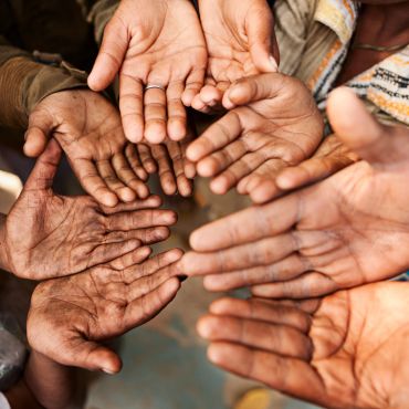 Multiple outstretched hands of diverse skin tones reaching upwards together.