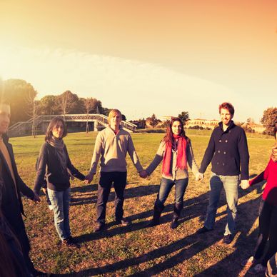 Group of people holding hands in a circle outdoors on a sunny day.