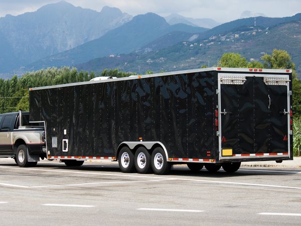 A black pickup truck towing a large black enclosed trailer in a parking lot.