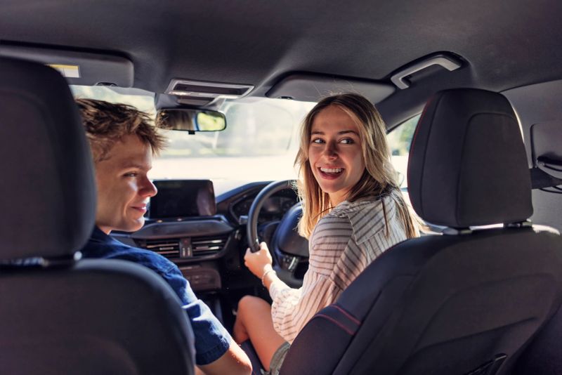 Teenagers having fun travelling by car. Teenage girl is driving the car and the boy is sitting next to her.Shot with Canon R5
