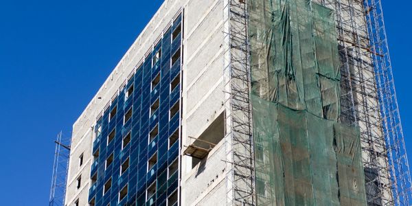 A high-rise building under construction with scaffolding and green netting.