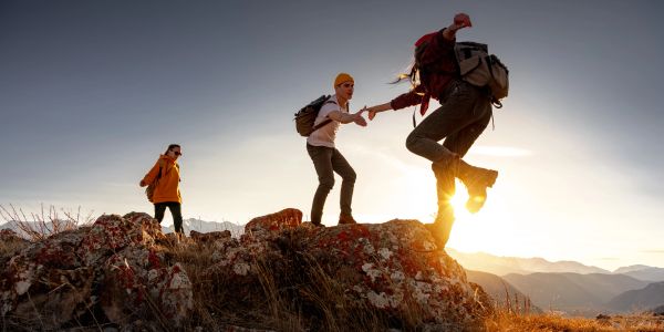 Three people hiking on rocky terrain at sunset.