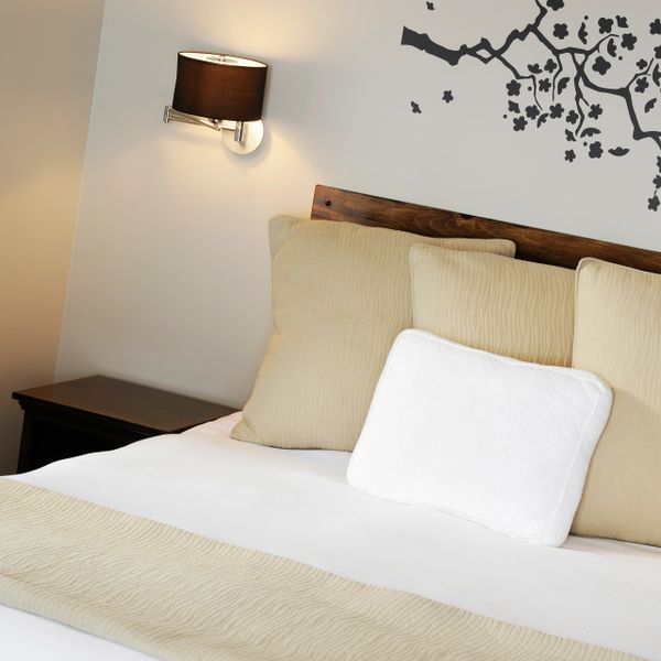 Cozy bedroom with beige pillows, white bedding, and a wall lamp.