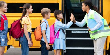 Children get a high-five from a bus driver.