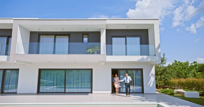 Agent showing a modern house to potential buyers on a sunny day.