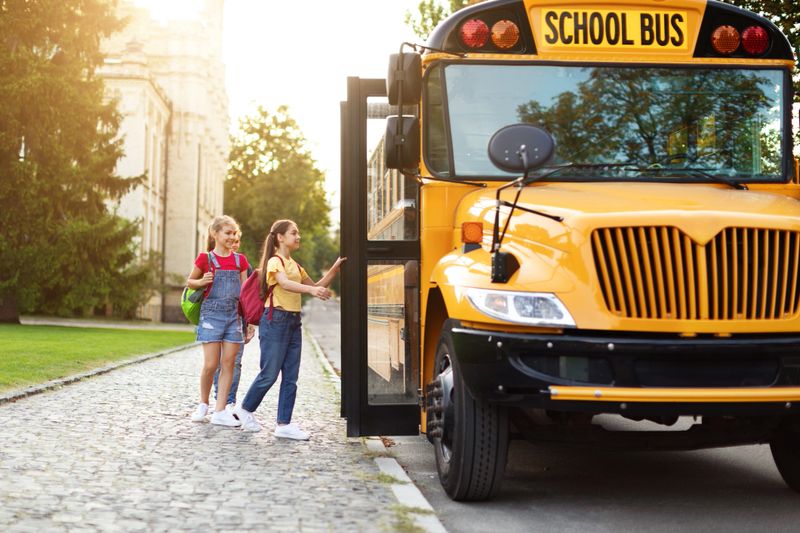 Group of happy kids boarding a yellow school bus after lessons, cheerful pupils with backpacks entering vehicle, group of children laughing and smiling, ready to go home, copy space