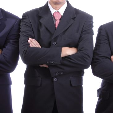 Hombres de negocios con brazos cruzados, vistiendo trajes formales.