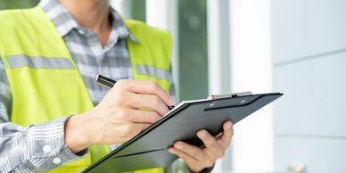 Worker in a safety vest writing on a clipboard outdoors.