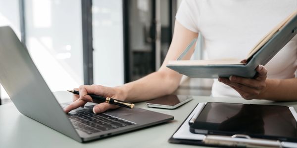 Person multitasking with laptop, book, and tablet on desk.