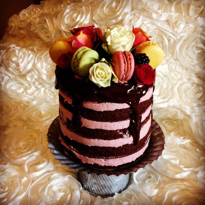 Elegant layered chocolate cake topped with roses, macarons, and berries.