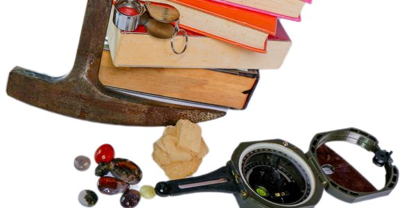 Geology tools including hammer, compass, loupe, and rock samples beside stacked books.