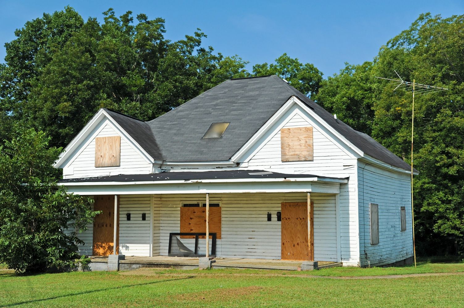 Abandoned house with boarded-up windows and doors surrounded by greenery.
