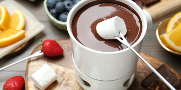 A marshmallow being dipped into creamy hot chocolate.