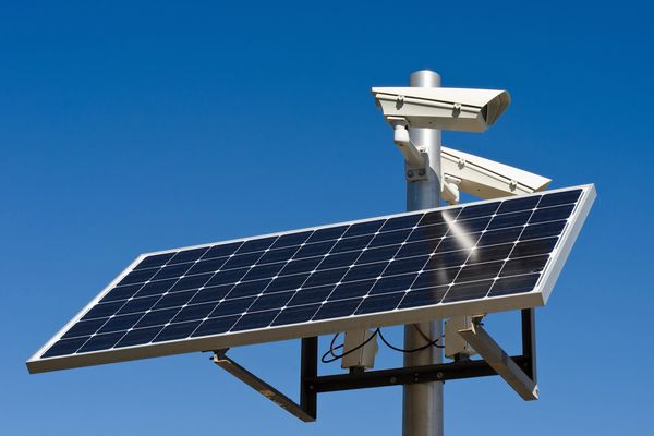 Solarmodul mit Überwachungskameras vor blauem Himmel.