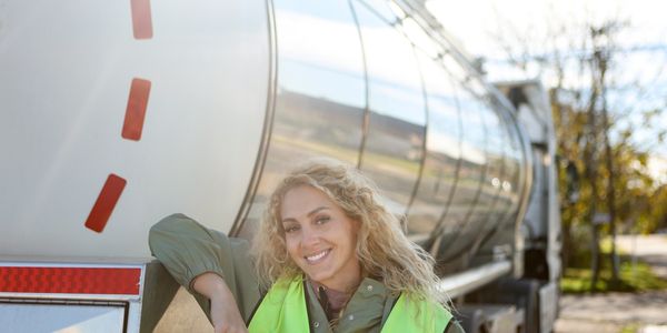 Female truck driver leaning on tanker truck symbolizing trucking career options