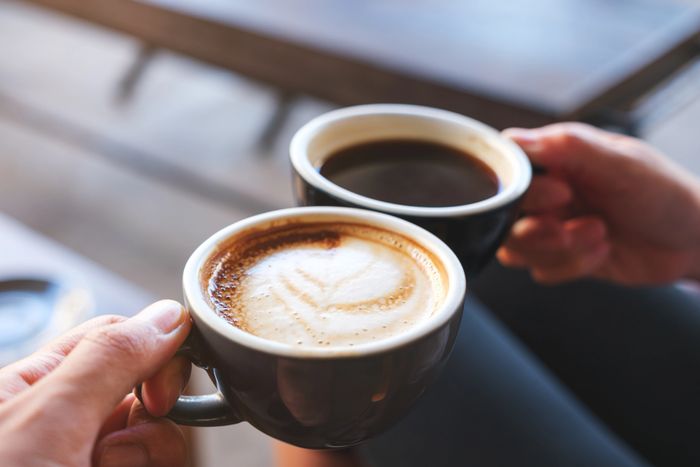 Two hands holding cups of coffee, one with latte art.