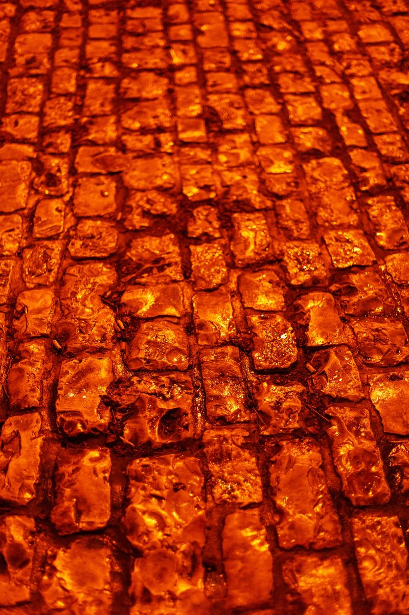 Shiny, colorful, cobblestone streets shimmer with artificial light following a rain storm and create an ideal, abstract texture for background illustration.