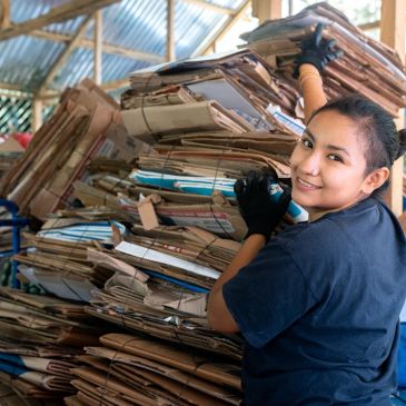 Mujer organizando paquetes de periódicos reciclados.