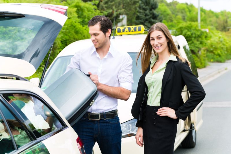 Young woman standing in front of taxi, she has reached her destination, the taxi driver will help with the luggage