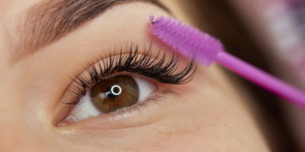 Close-up of eye with long eyelashes and a purple eyelash brush.