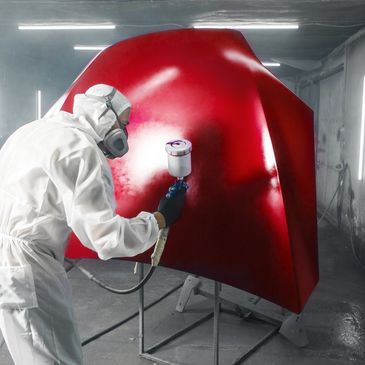 Person in protective gear spray painting a red car hood.