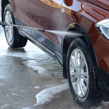 A person pressure washing a brown car's tire and side panel.