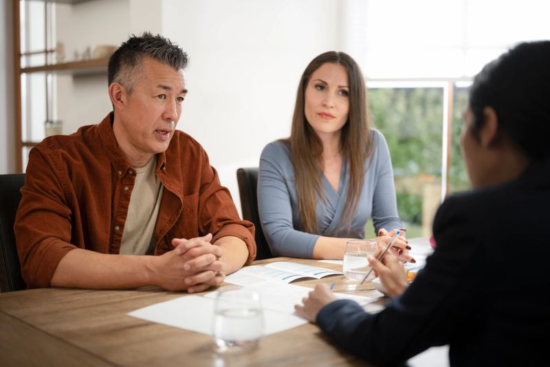 Mature couple talking with financial advisor while sitting at dining table in house.
