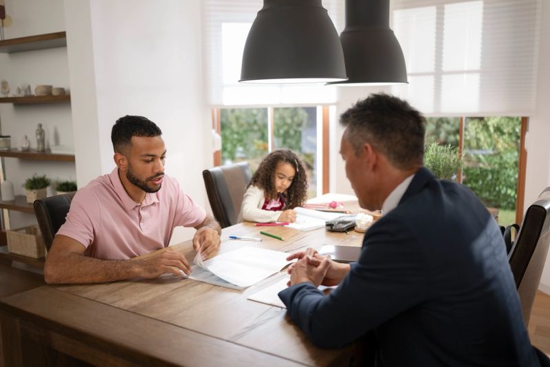 Male insurance adviser explaining document to customer as they sit at dining table.