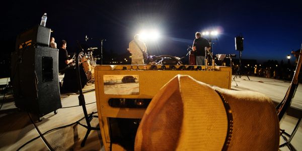 A nighttime outdoor concert with musicians performing on stage and a hat in the foreground.