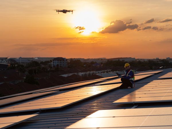 Person inspecting solar panels with a drone during sunset.