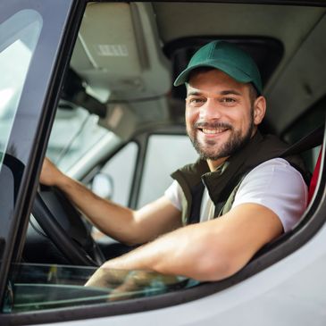 Smiling man in a green cap driving a vehicle, looking at the camera.