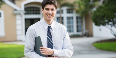 Smiling man in business attire holding a folder outside a house.