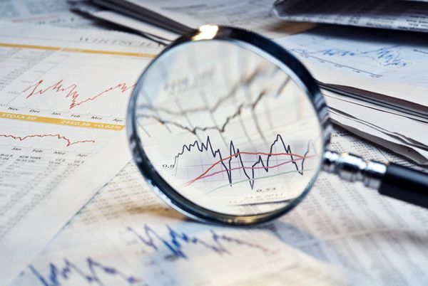 Magnifying glass focusing on financial graphs and stock market data.