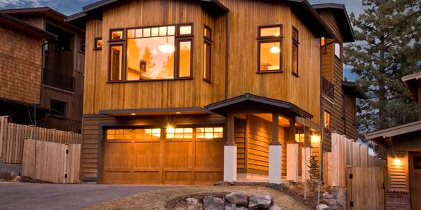 Modern two-story wooden house with warm interior lights glowing at dusk.