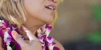 Woman with flower lei touching her neck.