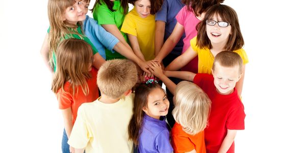 Children in colorful shirts join hands in a group circle, smiling and united.