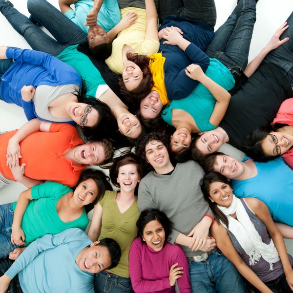 A diverse group of smiling young adults lying in a circle, heads together.