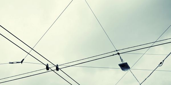 Overhead electric wires crisscross against a cloudy sky.
